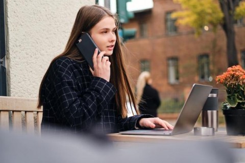Free photo attractive casual girl talking on cellphone and surfing internet on laptop in street cafe